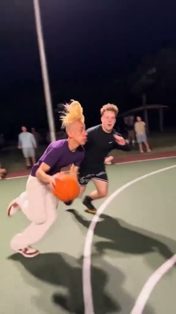 A player crossing over his defender on a floodlit court, from a viral Middle Finger Dunk video