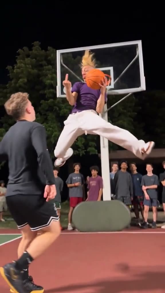 A player hanging on the rim over his defender, from a viral Middle Finger Dunk video